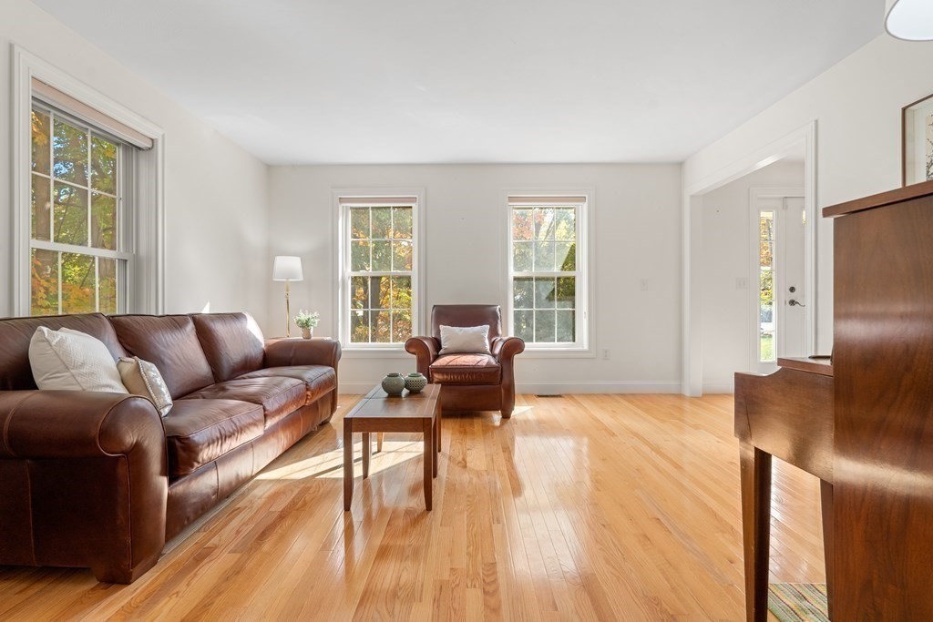 Living room with polished hardwood floors, leather seating, and tall windows overlooking autumn foliage.
