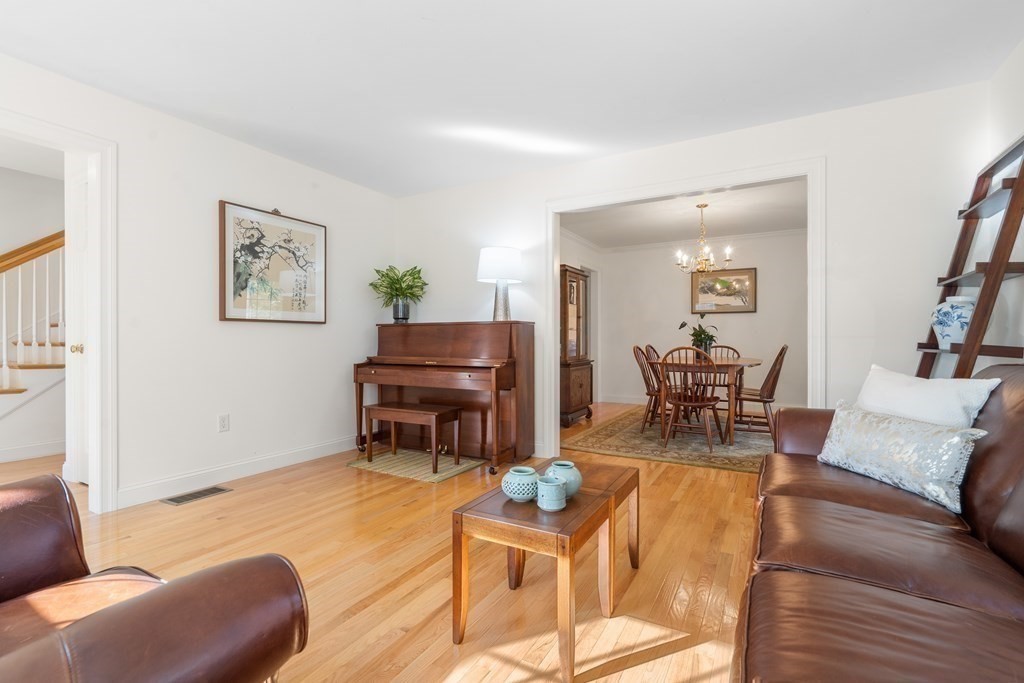 Living room with hardwood floors, leather sofas, a piano, and an adjoining dining area.
