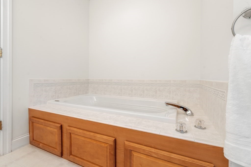 Bathroom soaking tub with tiled surround and warm wood cabinetry.