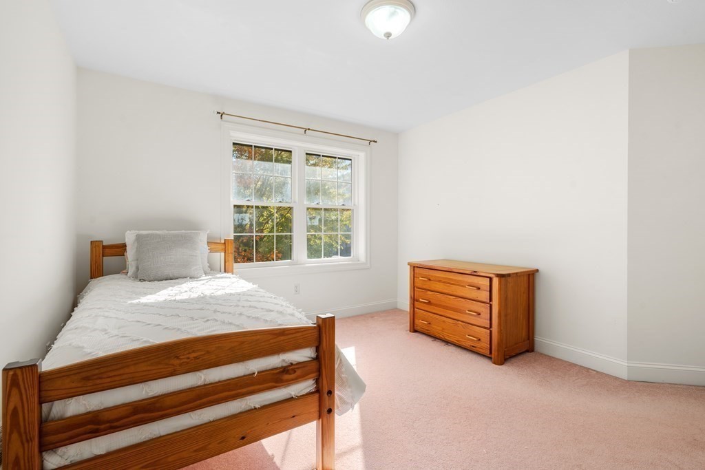 Bedroom with a wooden single bed, matching dresser, pink carpet, and a large window.