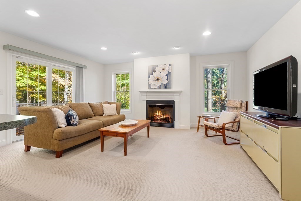 Living room with a tan sectional, lit fireplace, and large windows overlooking trees.