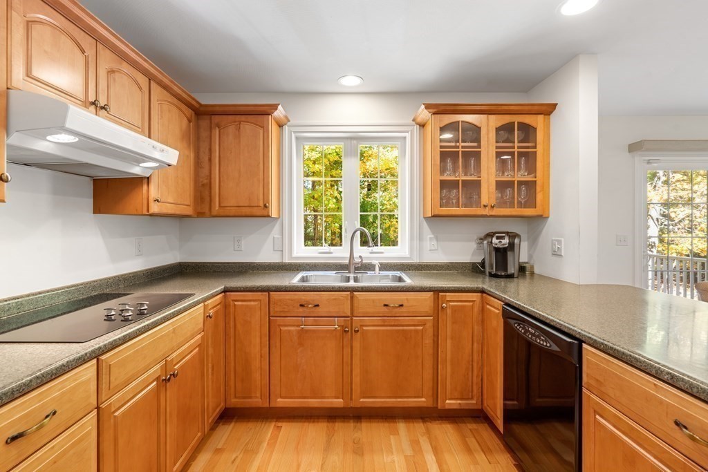 Kitchen with warm wood cabinets, granite countertops, and a sink beneath a window overlooking autumn foliage.