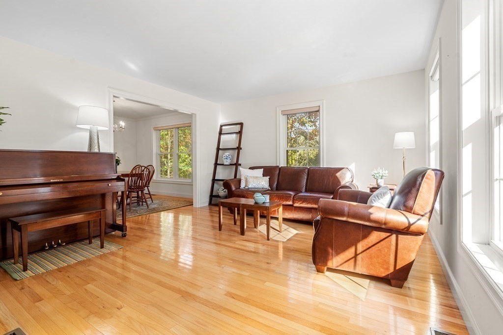 Living room with leather seating, a Baldwin piano, polished hardwood floors, and large sunny windows.