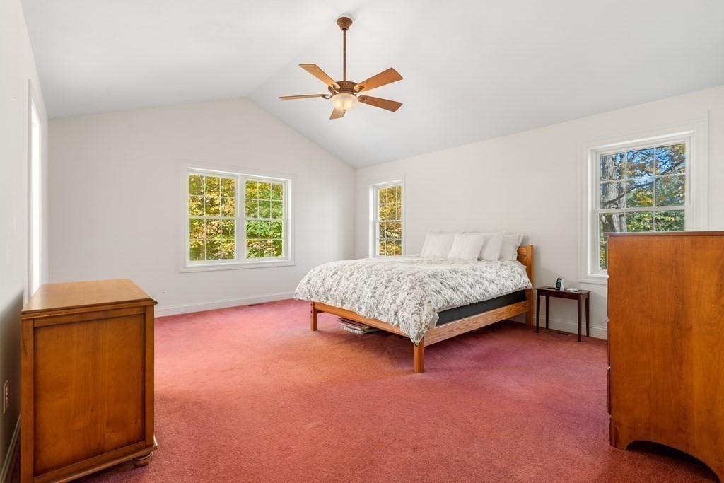 Bedroom with rose-colored carpet, a wooden bed, and windows overlooking trees.