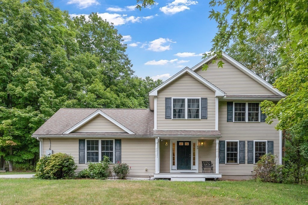 Two-story beige house with gray shutters, a covered entry, and a broad lawn.