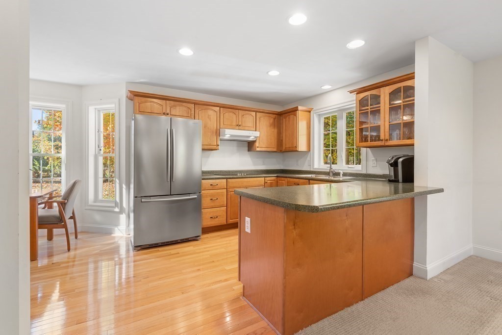 Kitchen with warm wood cabinets, stainless steel refrigerator, granite counters, and a large peninsula.