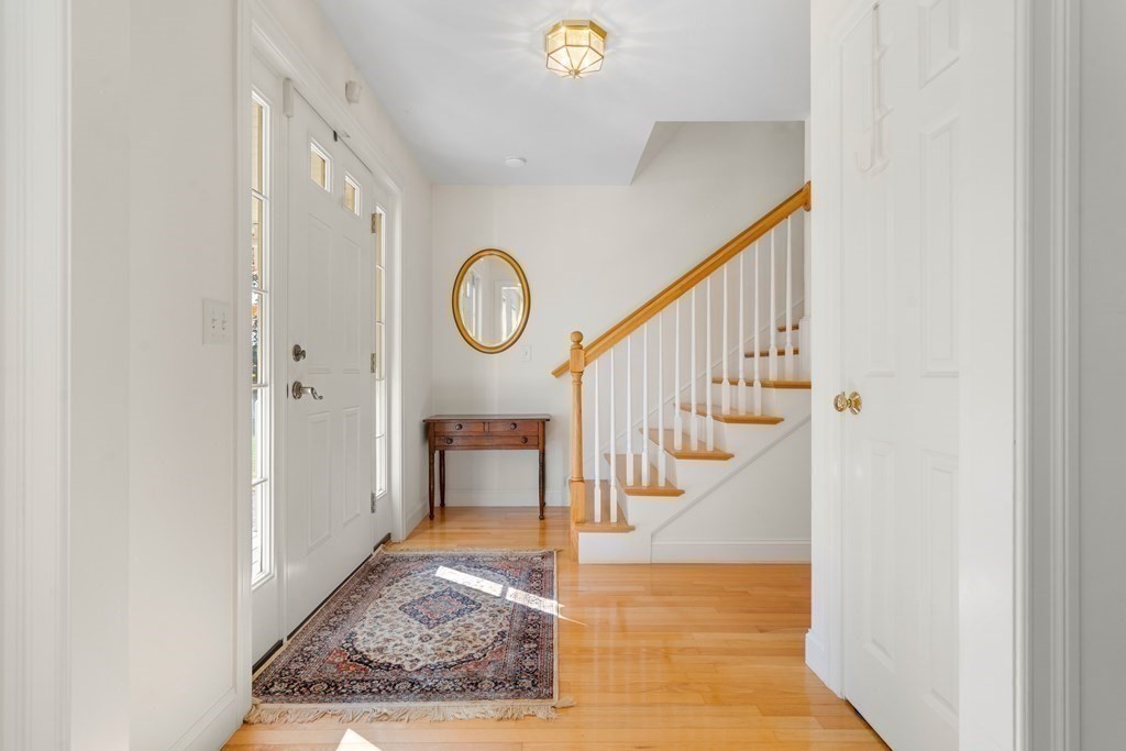 Entry foyer with hardwood floors, patterned runner, console table, and staircase with a wood railing.