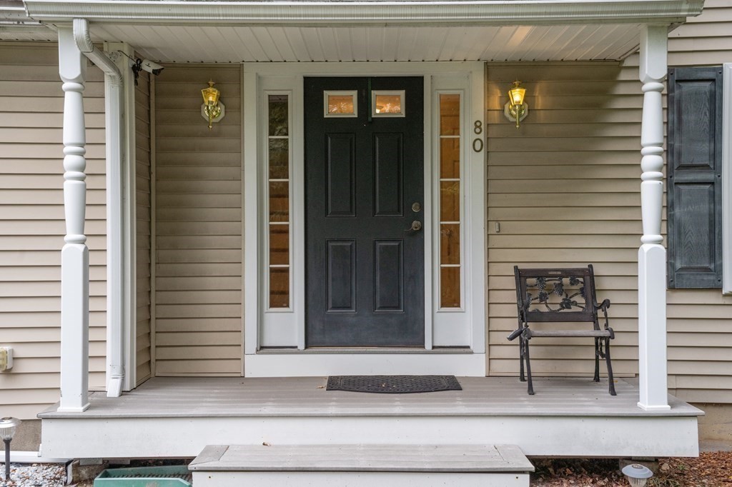 Front entrance with a black paneled door, narrow sidelights, white porch columns, and a metal chair.