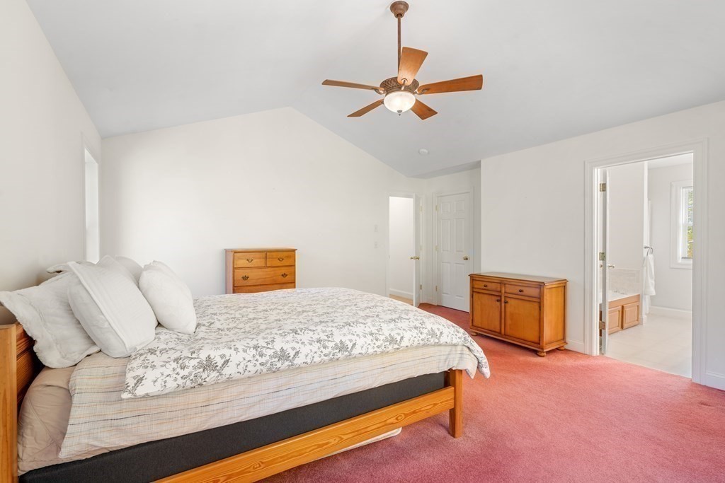 Bedroom with floral bedding, pink carpet, wooden dressers, and a ceiling fan.