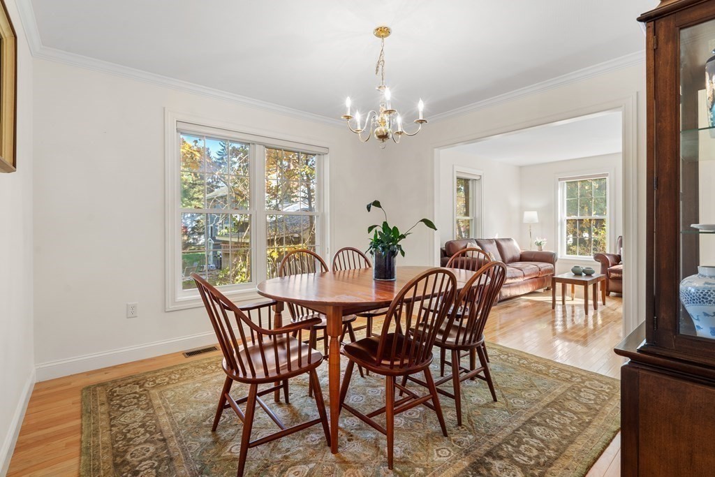 Dining room with a wooden table, patterned rug, chandelier, and open view into a furnished living room.