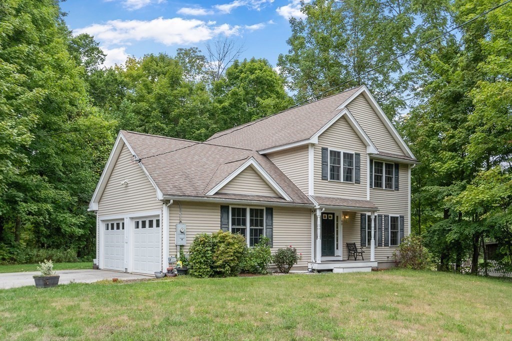 Two-story beige home with an attached garage, covered porch, and mature trees.