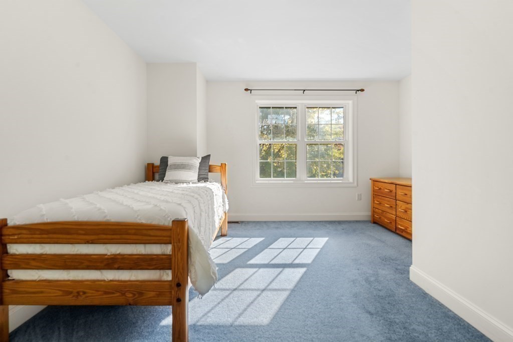 Furnished bedroom with a wooden bed, blue carpet, and sunlight coming through a large window.