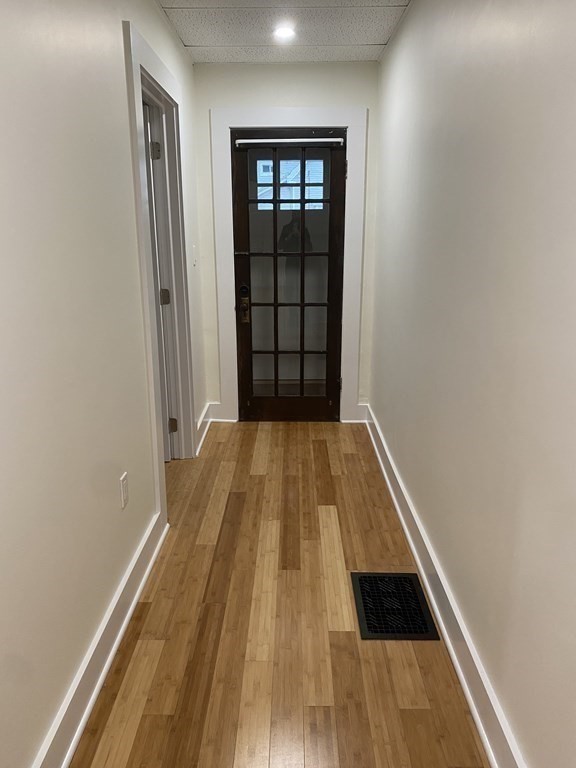 Narrow hallway with wood flooring leading to a dark, multi-pane glass door.