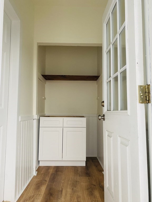 Narrow alcove with a white cabinet, dark wood shelf, and open glass-paneled door.