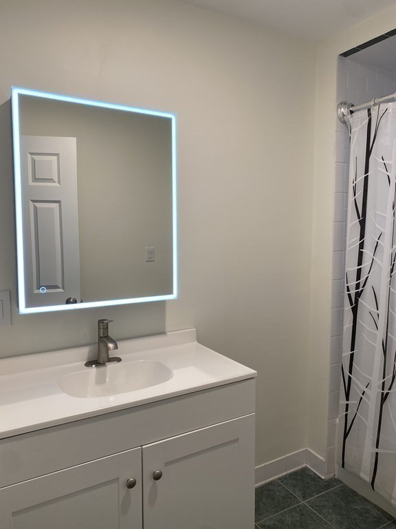 Bathroom with a white vanity, illuminated mirror, and black-and-white patterned shower curtain.