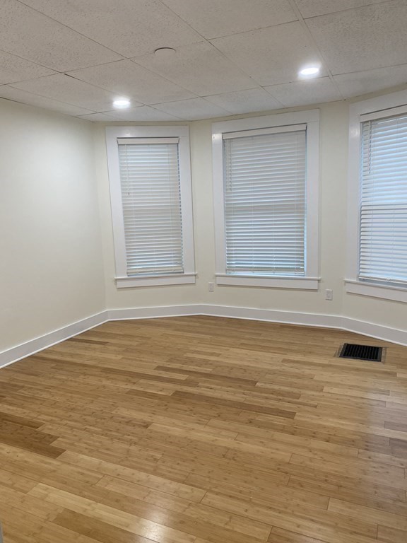 Empty room with hardwood floors, three windows with blinds, and recessed lighting.