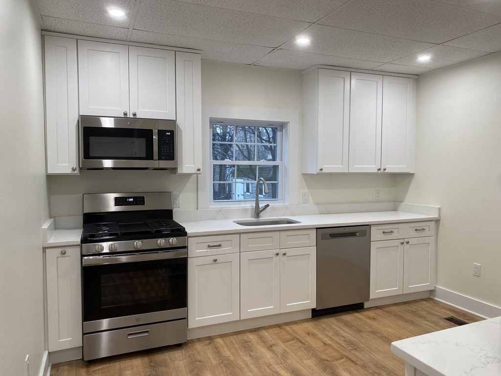 Renovated kitchen with white cabinets, stainless steel appliances, and a window above the sink.