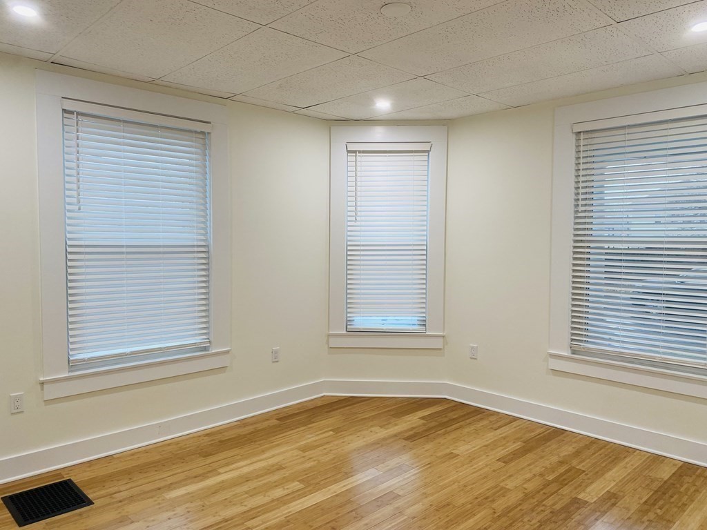 Empty room with hardwood floors and three windows with blinds.