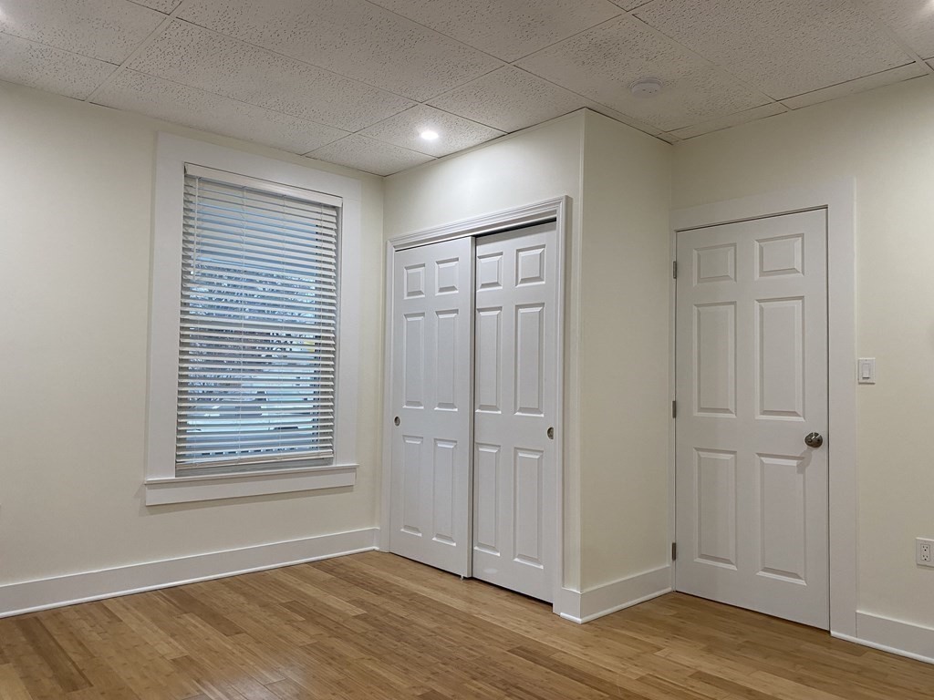 Empty room with hardwood floors, a window with blinds, and a double closet.