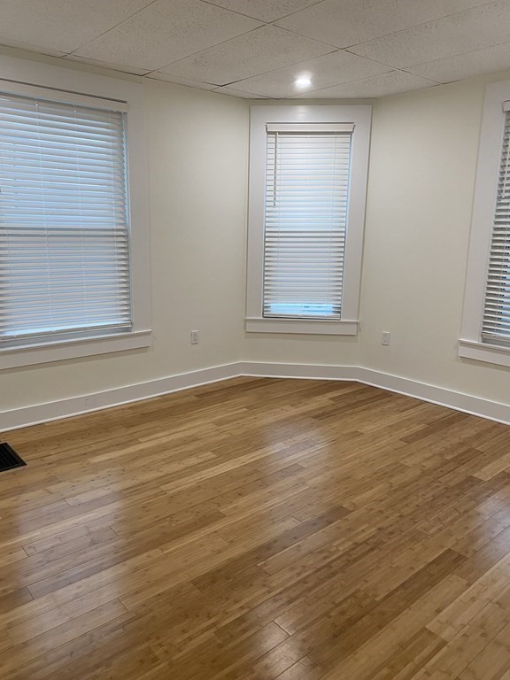 Empty room with polished hardwood floors and three windows with blinds.