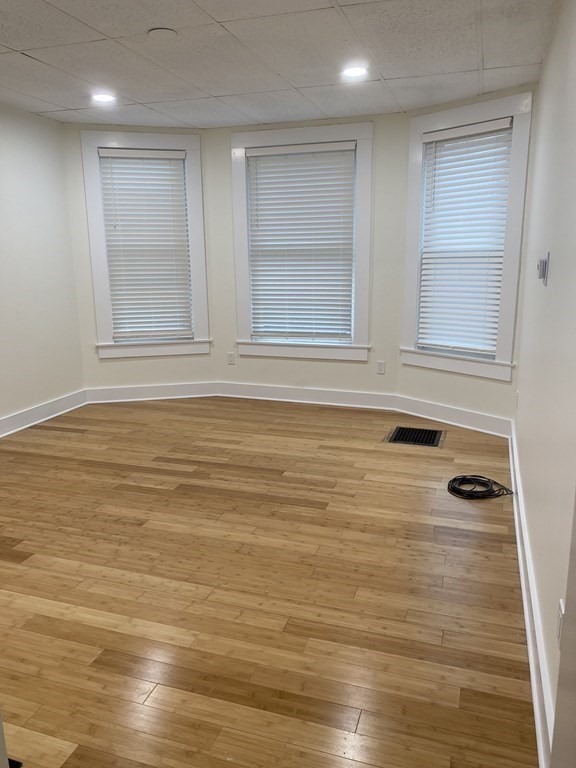 Empty room with hardwood floors and three windows with blinds.