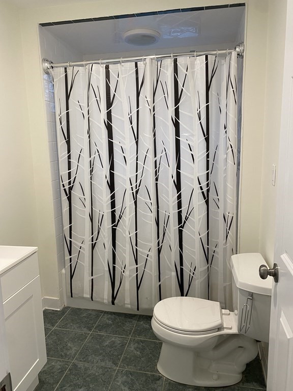 Bathroom with a branch-patterned shower curtain, toilet, dark green floor tiles, and white vanity.