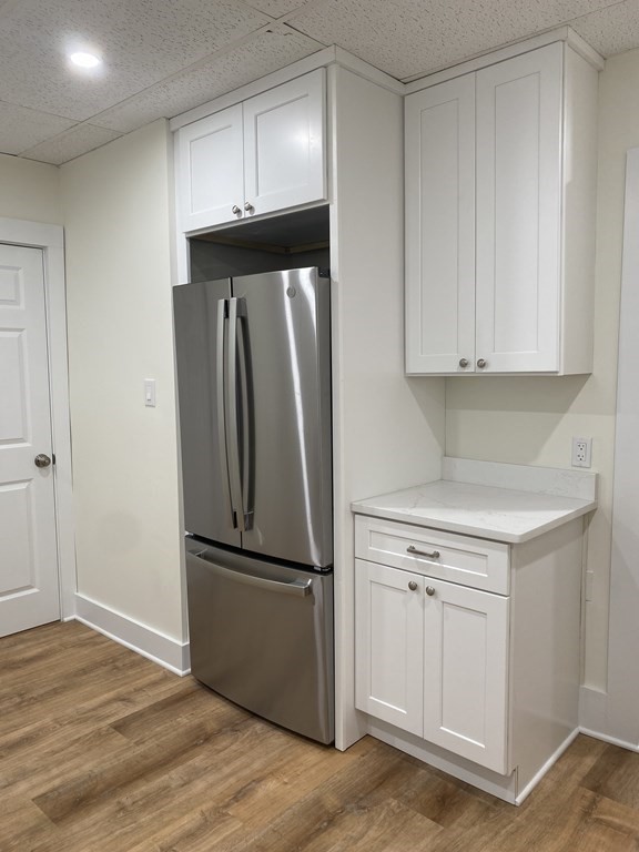 Kitchen corner with a stainless-steel refrigerator, white cabinets, and a marble-look countertop.