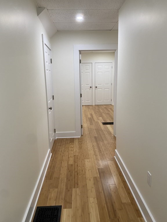Empty hallway with light wood floors, white walls, and multiple doors.
