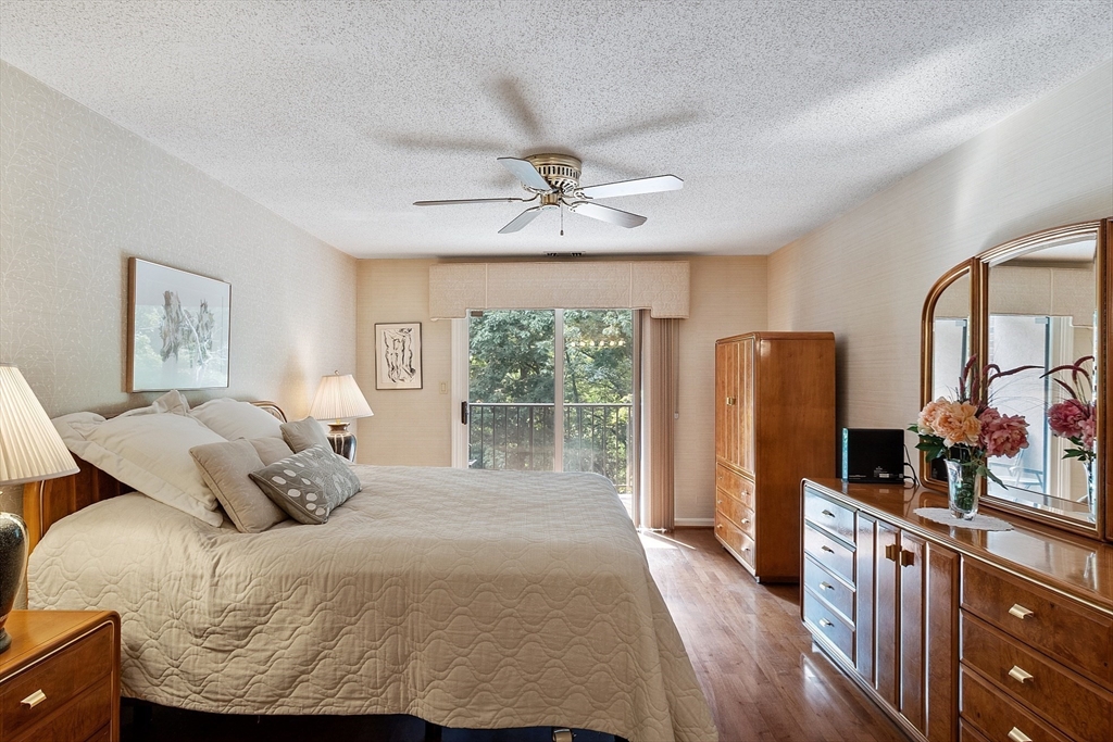 Bedroom with a large bed, wooden dressers, and sliding doors to a tree-lined balcony.