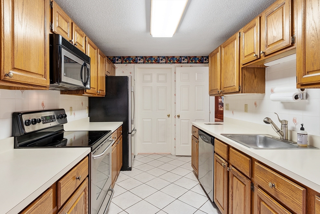 Kitchen with honey-colored wood cabinets, white counters, and a stainless-steel sink.
