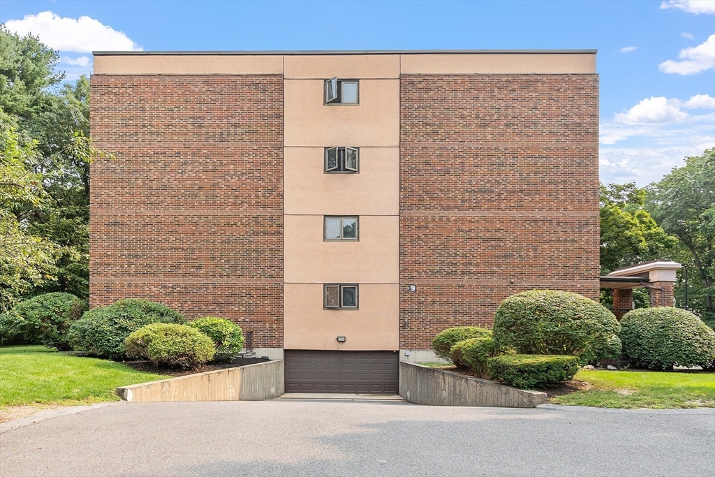 Brick residential building with a tan central facade, garage entrance, and landscaped shrubs.