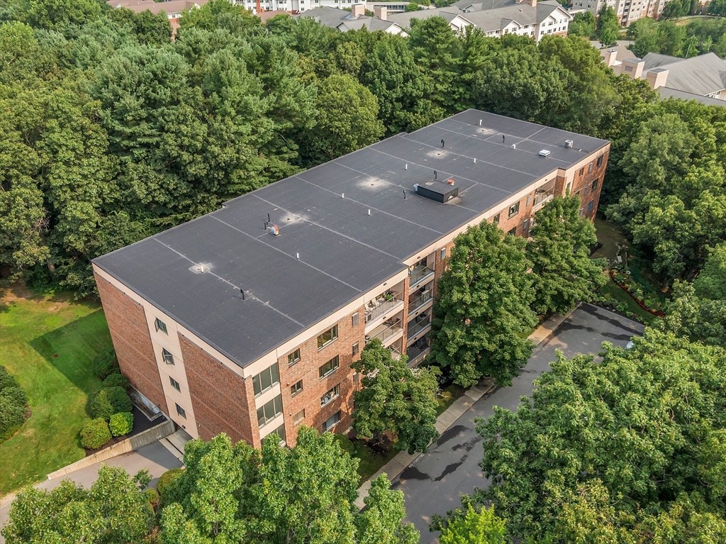 Aerial view of a brick condominium building surrounded by mature trees, with balconies and a large flat roof.