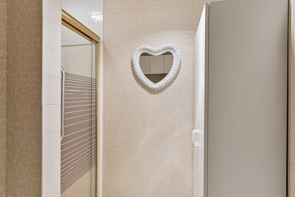 Bathroom shower with beige patterned walls and a white heart-shaped mirror.