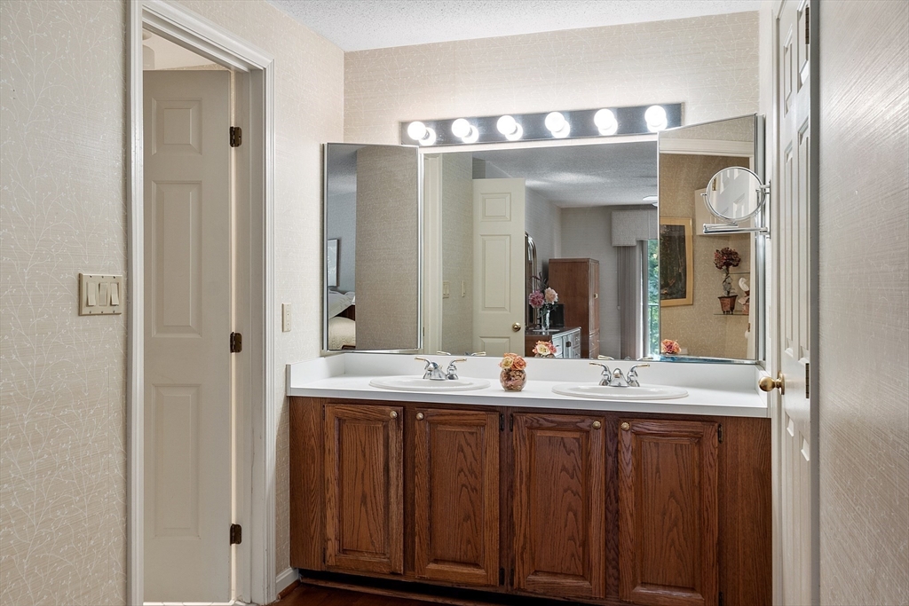 Bathroom with a double-sink vanity, dark wood cabinets, and a wide mirror with lights.