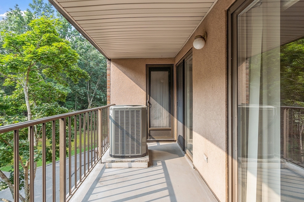 Covered balcony with sliding glass doors and an air-conditioning unit overlooking leafy trees.