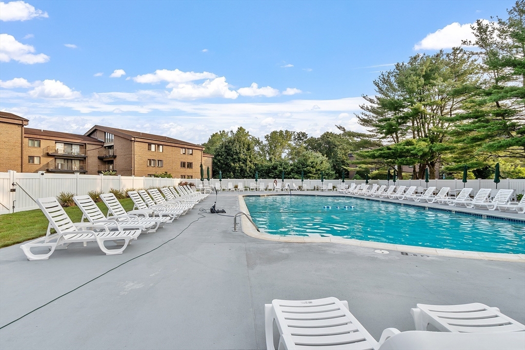 Outdoor swimming pool surrounded by white lounge chairs beside brick residences.