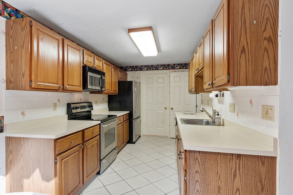 Galley kitchen with oak cabinets, white countertops, and stainless steel appliances.