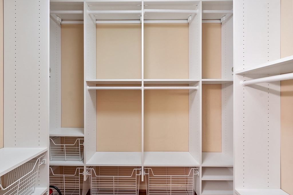 Walk-in closet with white built-in shelving, hanging rods, and pull-out wire baskets.