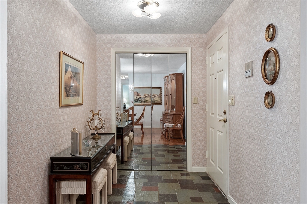 Entry hallway with patterned wallpaper, slate tile flooring, and mirrored doors opening to a dining room.