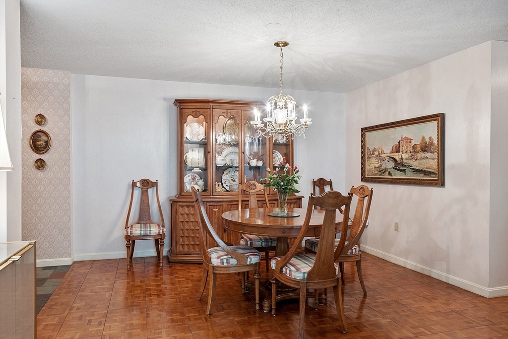 Dining room with a round wooden table, chandelier, china cabinet, and parquet floor.