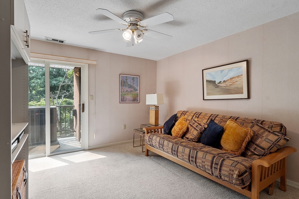 Living room with a patterned futon and sliding glass door opening to a tree-lined balcony.