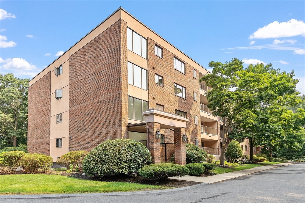 Multi-story brick condominium building with balconies and a landscaped entrance.