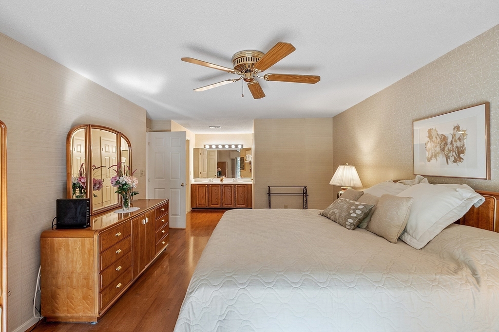 Furnished bedroom with a large bed, wooden dresser, arched mirror, and ceiling fan.