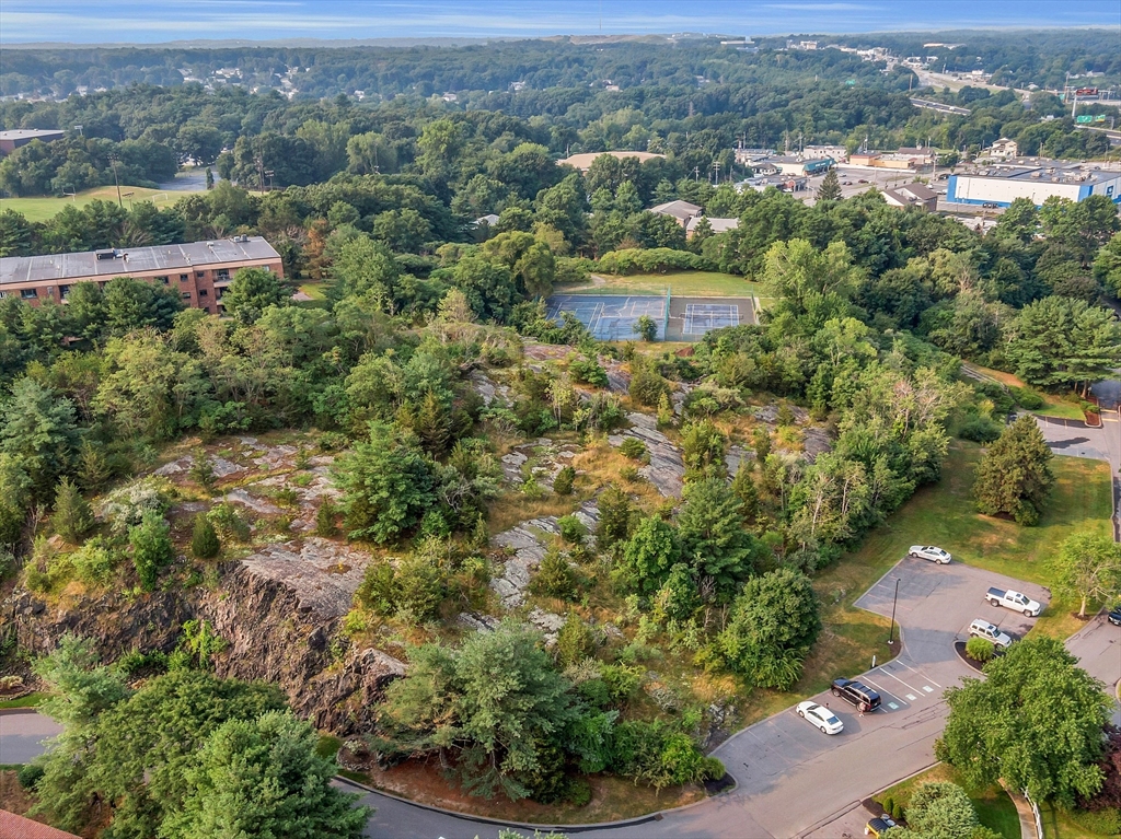 Aerial view of wooded grounds with a rocky ledge, tennis courts, and nearby parking.