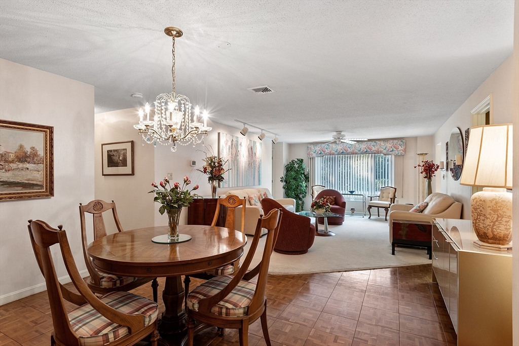 Open-plan dining and living room with a round wooden table, chandelier, and sitting area by the window.