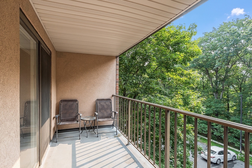Covered balcony with two chairs and a leafy treetop view.