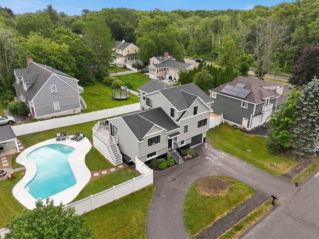 Aerial view of a gray multi-level home with a fenced swimming pool and wooded surroundings.