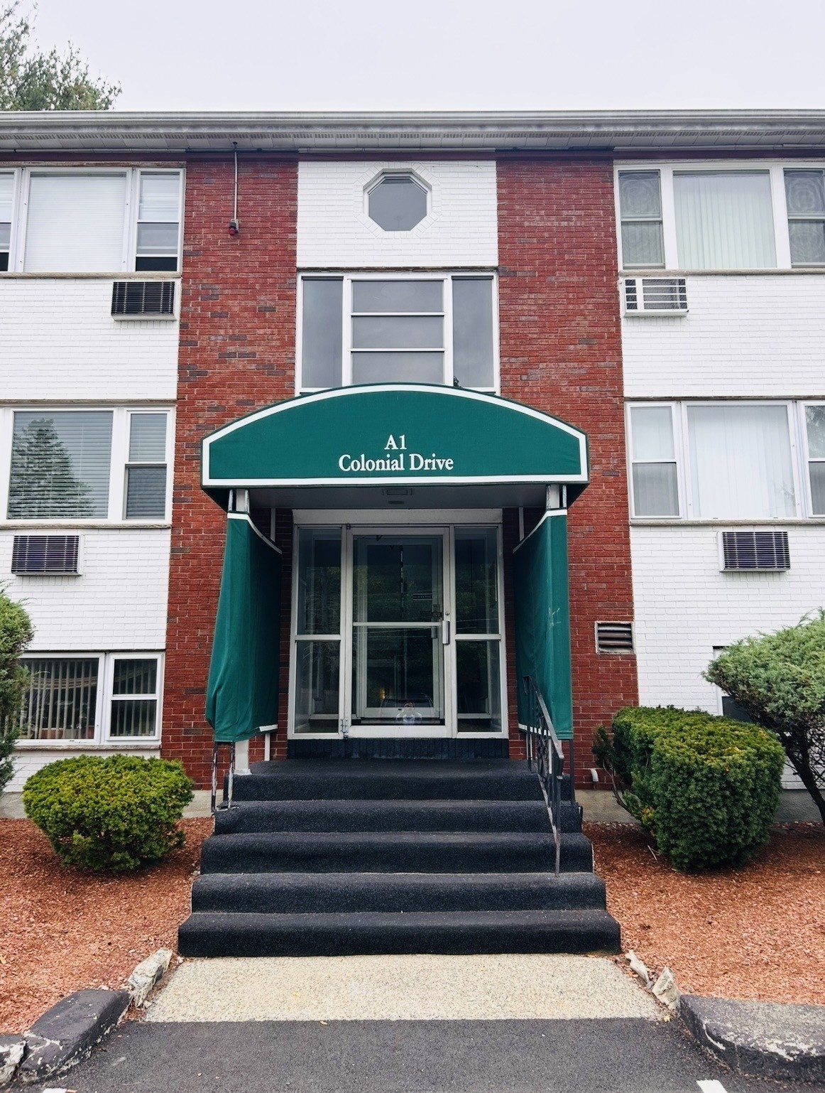 Apartment building entrance with a green “A1 Colonial Drive” awning and broad steps.