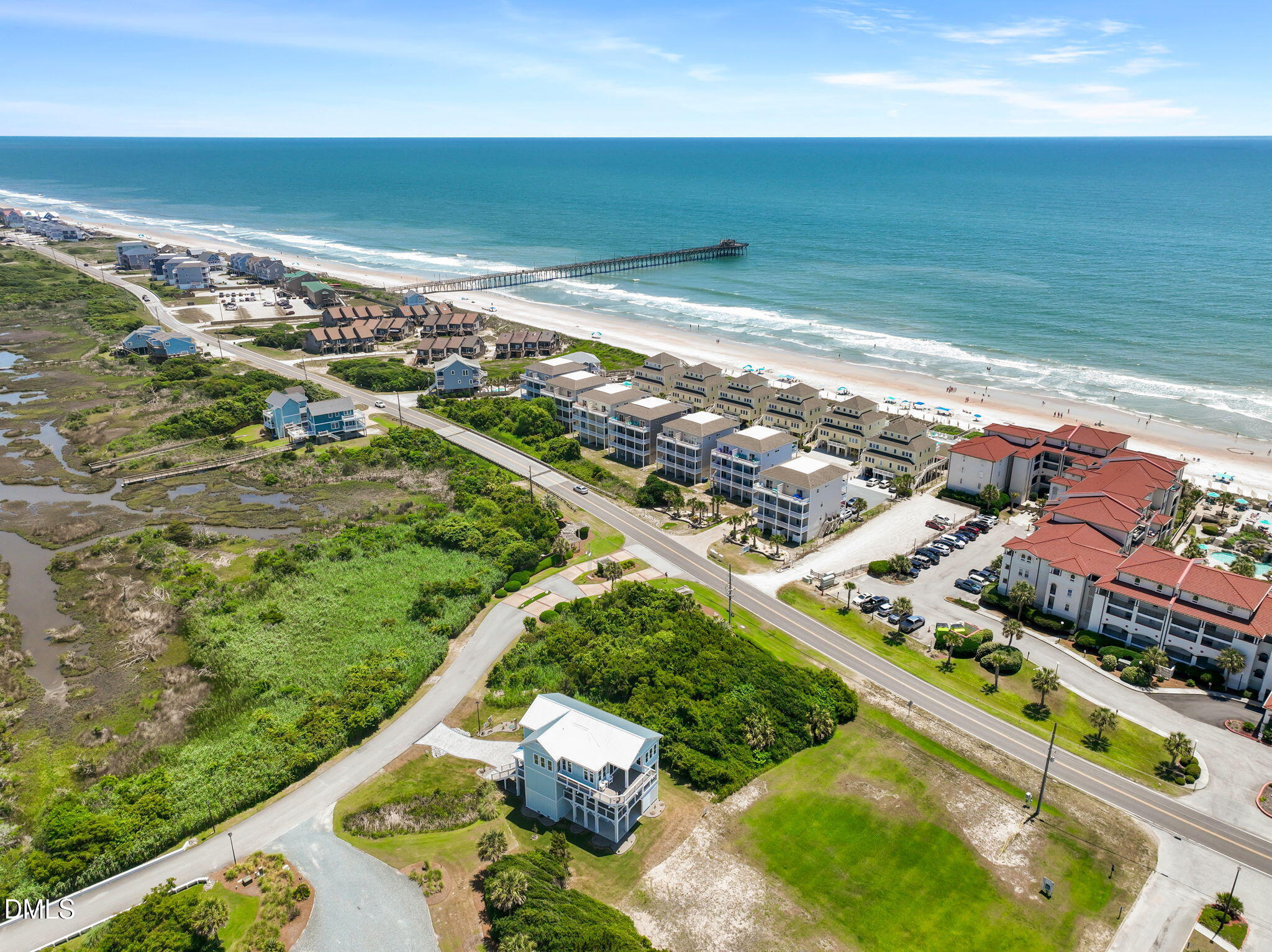 Blue coastal home beside marshland, with the beach, ocean, and pier beyond.