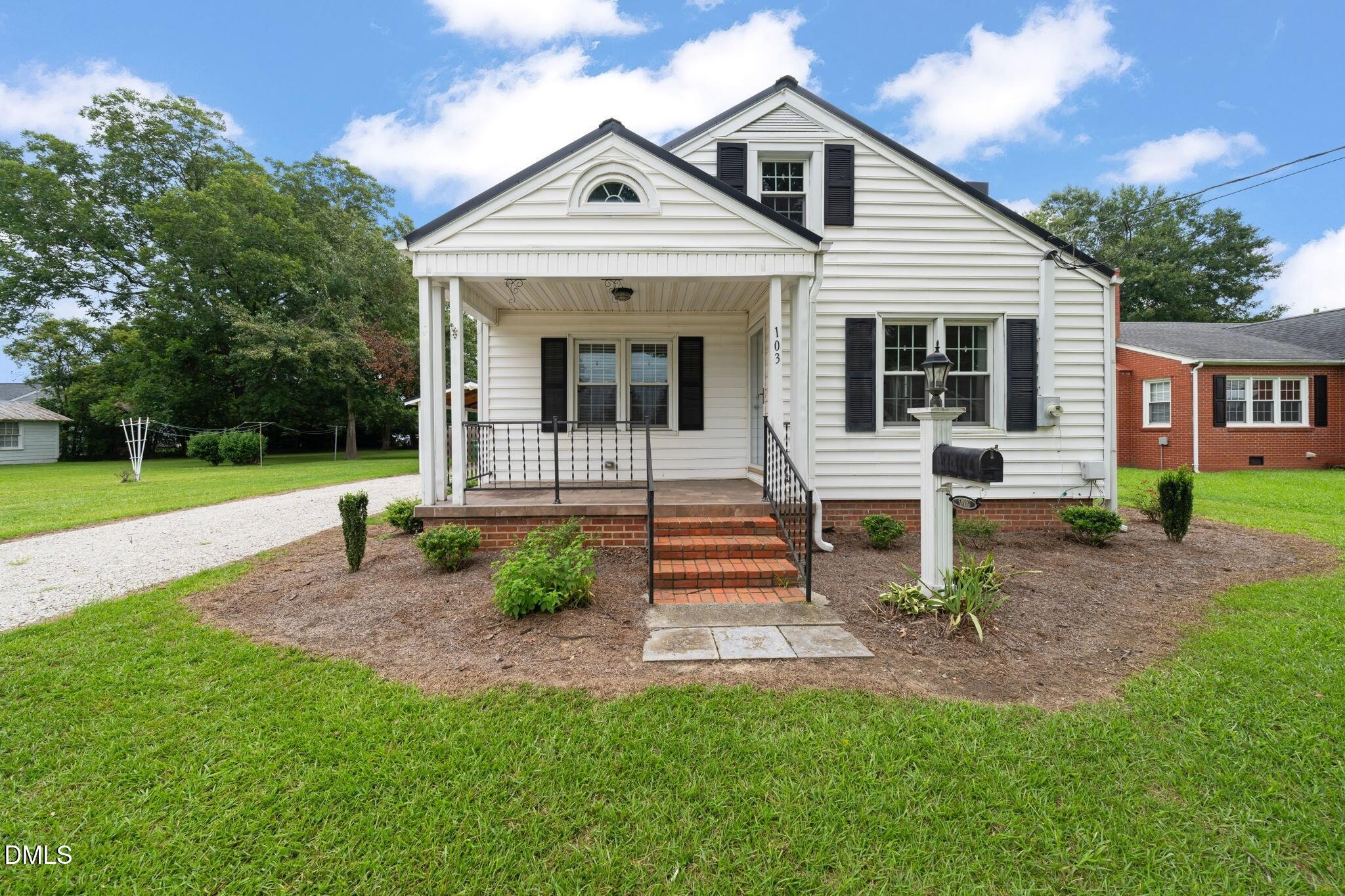 White home with black shutters, covered front porch, and brick steps leading to a green lawn.